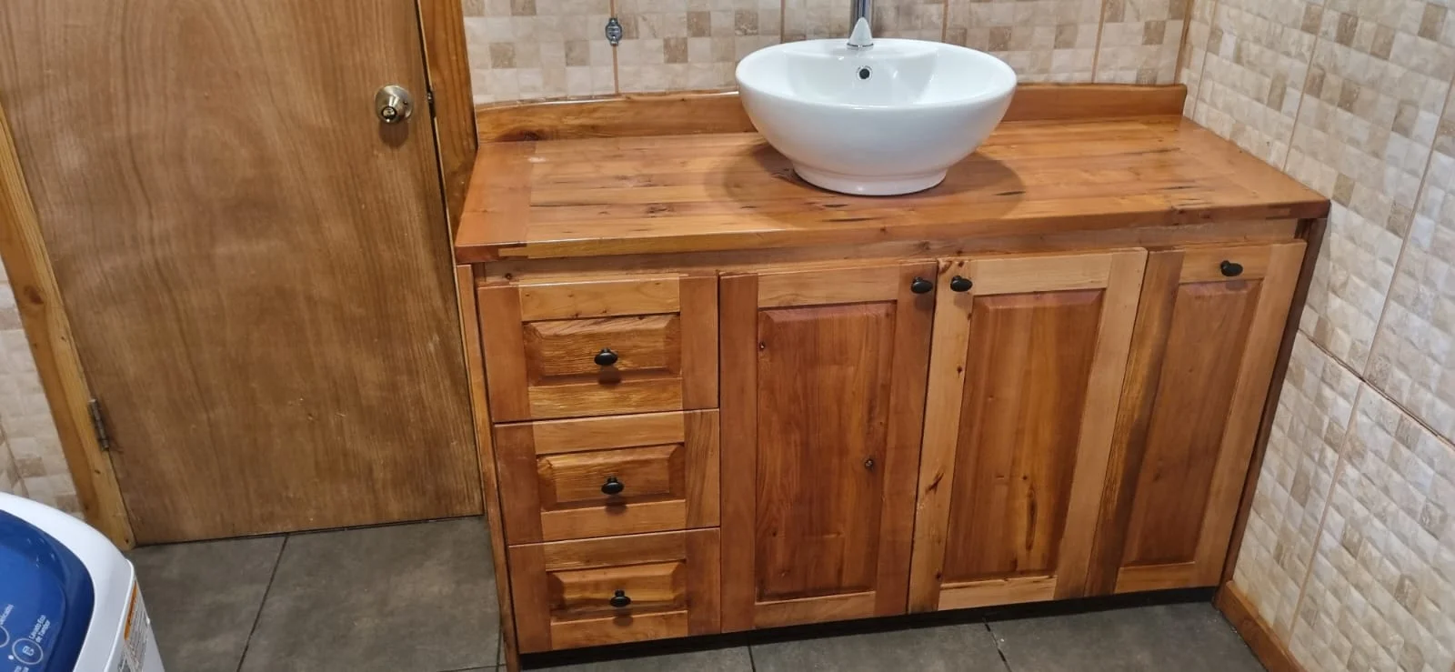 Vanitorio de baño a medida en madera nativa con cuatro cajones laterales, dos puertas batientes y mesada maciza con bowl cerámico blanco